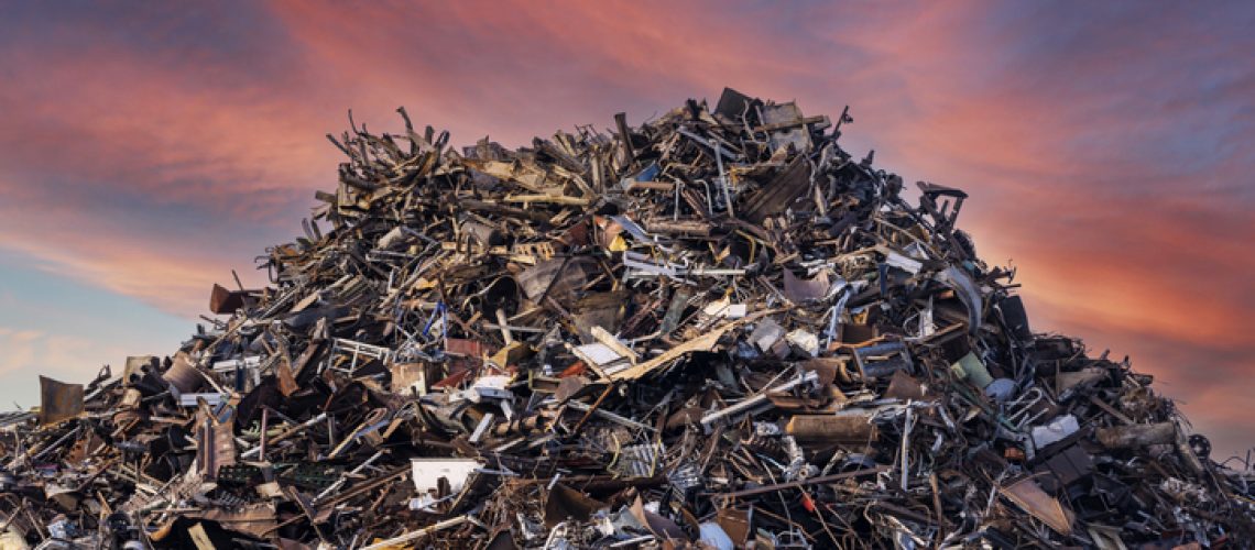 scrap metal heap at recycling junk yard against red sky at sunset